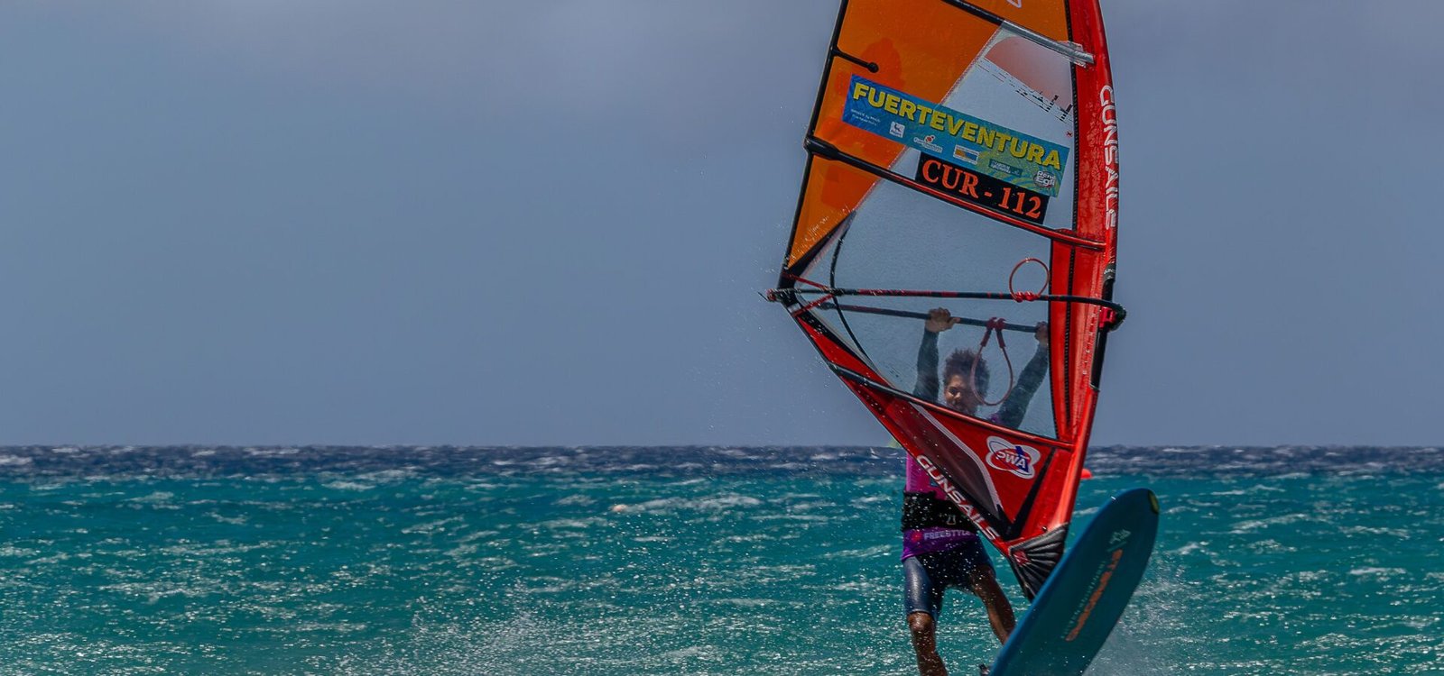 Un windsurfeur en plein virage, aileron et planche visibles sous l'eau