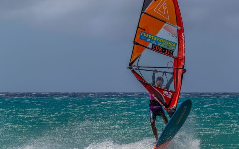 Un windsurfeur en plein virage, aileron et planche visibles sous l'eau