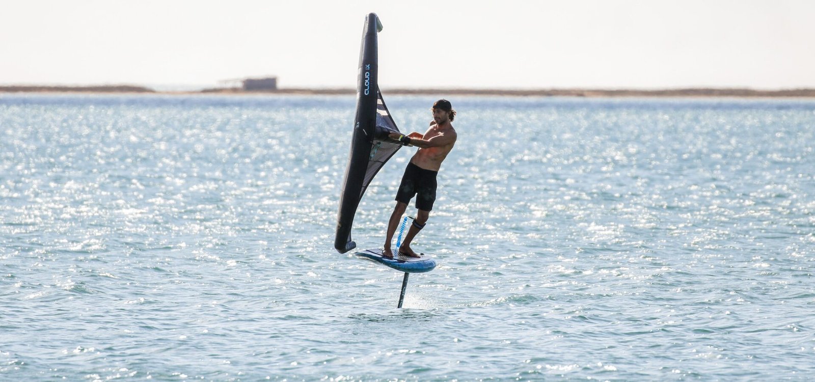 Un rider de wing foil tenant son aile à la main au-dessus de l'eau