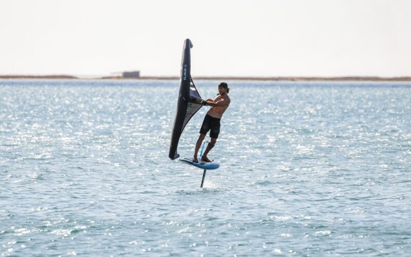 Un rider de wing foil tenant son aile à la main au-dessus de l'eau